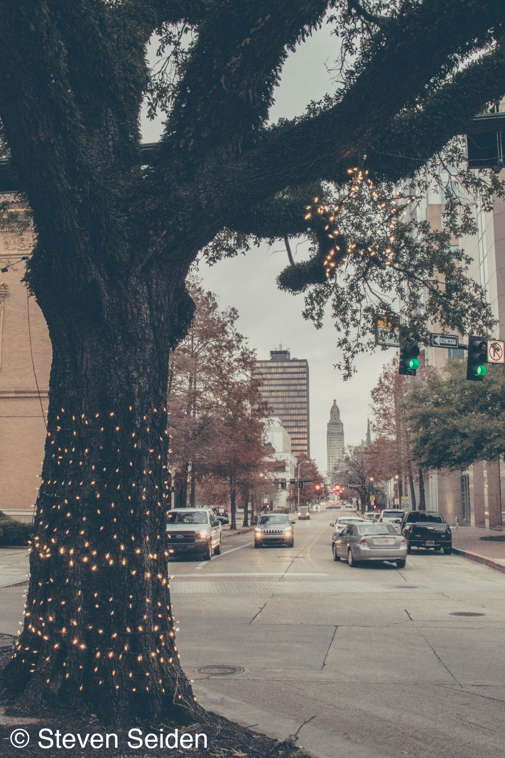 A picture of a downtown street with Christmas lights adorning a tree.