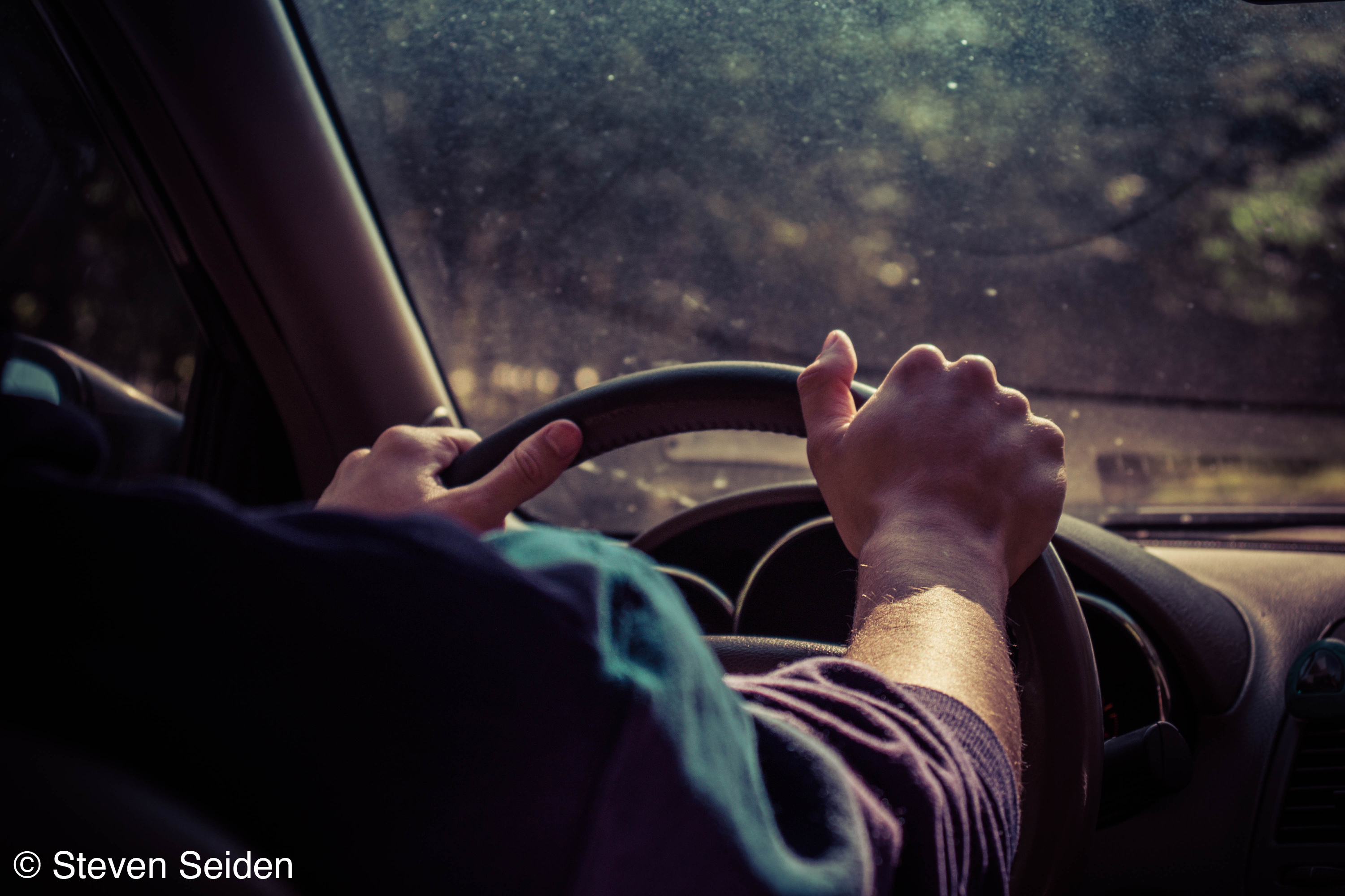 A picture of someone's hands on a car's steering wheel.